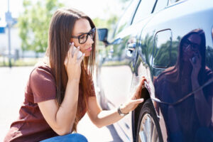 woman inspecting her car and calling insurance company