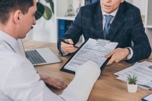 Businessman In Blue Jacket Giving Form For Compensation Claim To An Injured Man