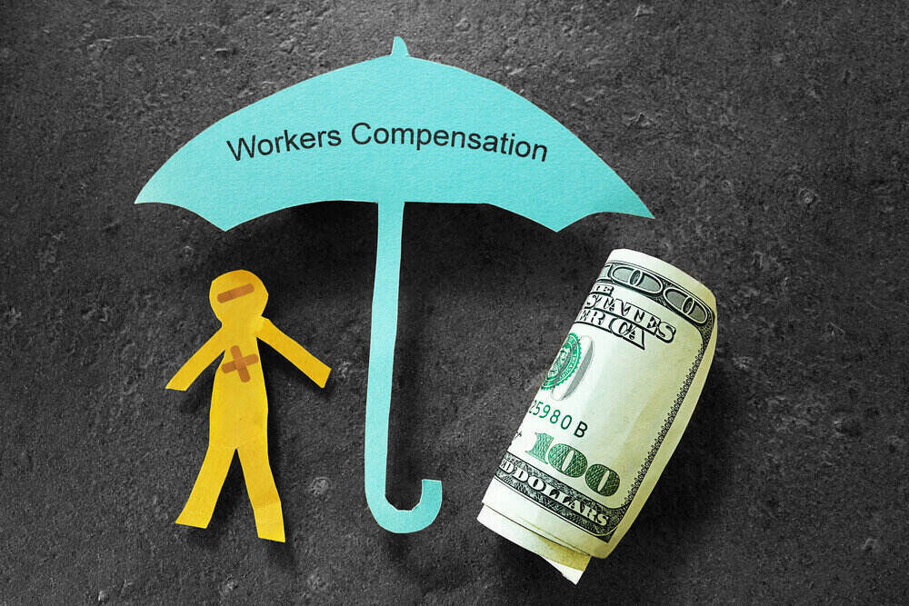 Paper man under a workers' comp umbrella with money next to him