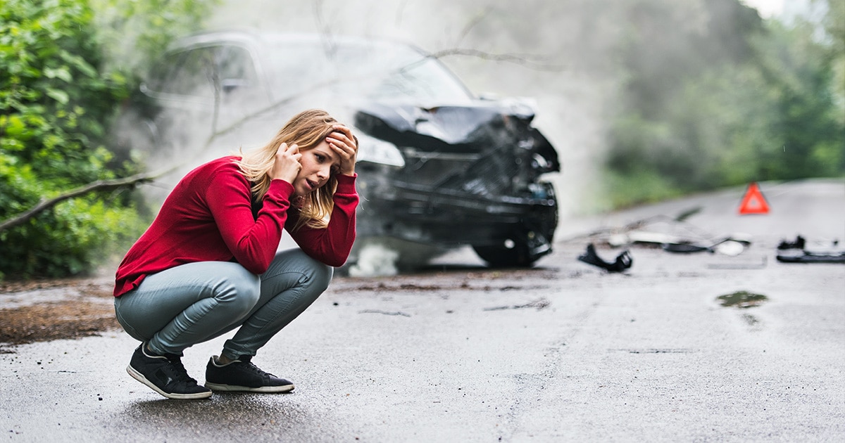 girl on the phone panicked standing beside her wrecked car