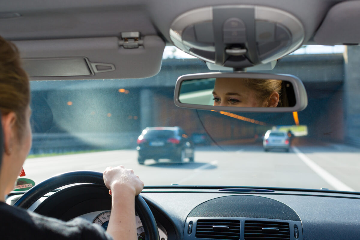 Lady driving a car about to go under a bridge. See her through the review mirror