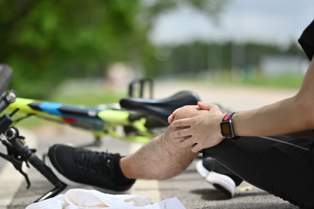 injury cyclist holding knee with bicycle