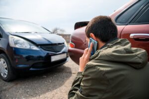 Person calls for assistance near two damaged cars after an accident, seeking legal or emergency help.